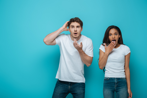 shocked man and african american girl looking at camera on blue background - Foto, imagen