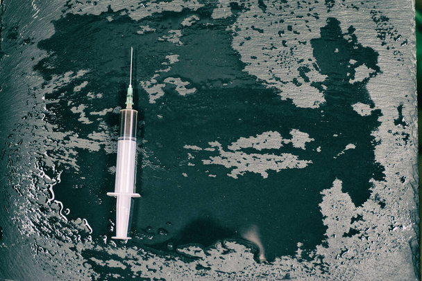 Syringe with a dark liquid on a dark wet background. - Photo, Image