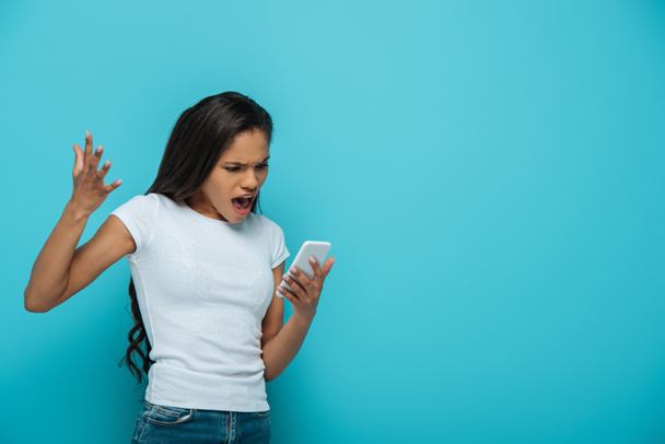 angry african american girl screaming during video call on smartphone isolated on blue - Fotoğraf, Görsel