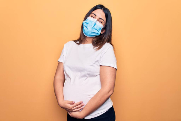 Jovem grávida mãe para estar usando máscara de proteção para coronavírus doença abraçando-se feliz e positivo, sorrindo confiante. Auto amor e auto cuidado
 - Foto, Imagem