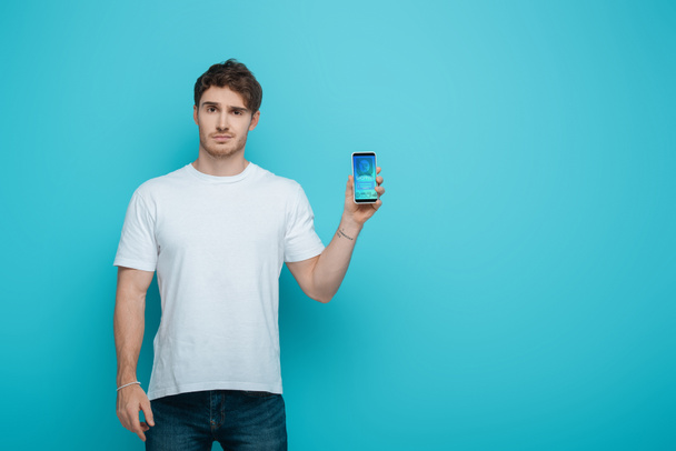 displeased young man showing smartphone with online shopping app on screen on blue background - Фото, зображення