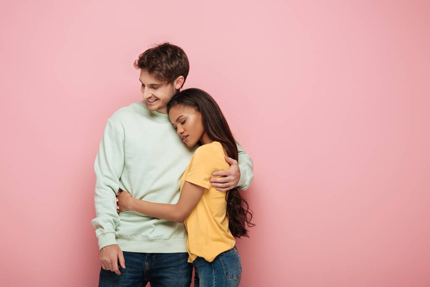 atraktivní africká americká dívka se zavřenýma očima a šťastný chlap objímající na růžovém pozadí - Fotografie, Obrázek