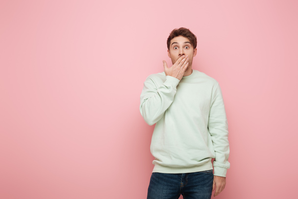 shocked man covering mouth with hand while looking at camera on pink background - Photo, Image