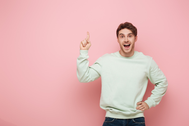 excited guy showing idea sign while standing with hand on hip and looking at camera on pink background - Fotó, kép