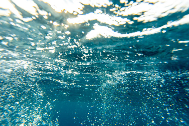 Υποβρύχιο φόντο του βαθύ τυρκουάζ και μπλε νερό του ωκεανού με ακτίνες του ήλιου διαθλαστική μέσα από την επιφάνεια. - Φωτογραφία, εικόνα