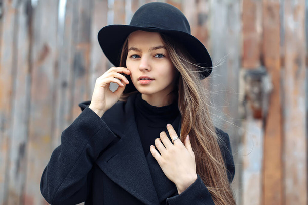 Young beautiful fashionable woman in black hat, with long hair posing on woody background. Female fashion, beauty concept. Outdoor. - Photo, image