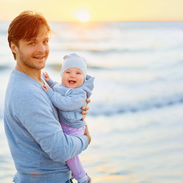 man with a smiling child in his arms on a sunset background - Photo, image