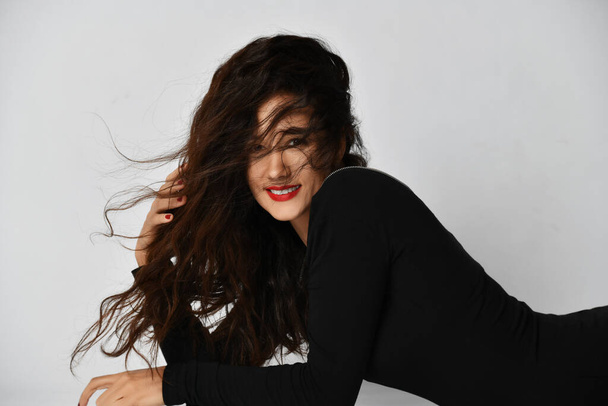 Woman in black tight dress half-lying on the floor with her with long curly brunette hair covering her face  - Foto, imagen