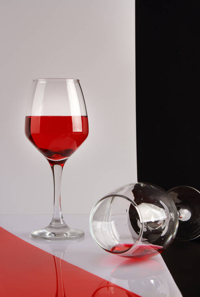 Still life with two glasses of red wine on a white glossy table and a black and white background - Foto, Imagen