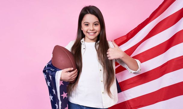 Funny stylish young emotional girl, long-haired brunette, smiles broadly and joyfully holds the American flag and ball, shows Like, ok,Independence Day,July 4,victory,peace, USA, on a pink background. - Zdjęcie, obraz