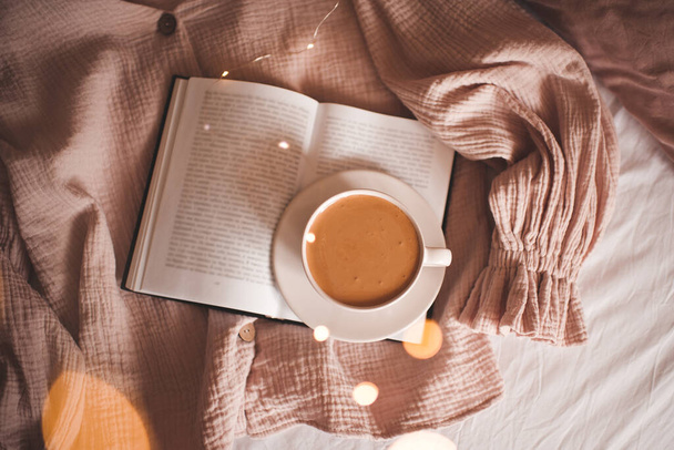 Tasse leckeren Kaffee auf aufgeschlagenem Buch im Bett Nahaufnahme. Ansicht von oben. Guten Morgen.  - Foto, Bild