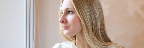 Beautiful blonde girl thoughtfully look out window - Foto, imagen