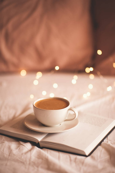 Xícara fresca de café em livro de papel em casa na cama closeup. Bom dia.
.  - Foto, Imagem