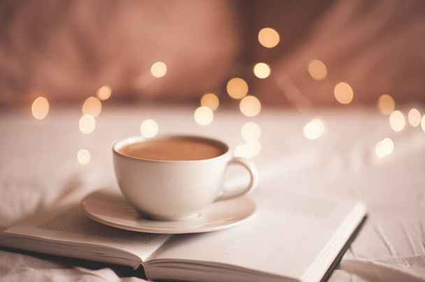 輝くライトの上に紙の本のコーヒーの新鮮なカップを閉じます。おはようございます.  - 写真・画像