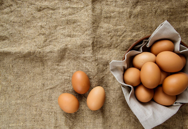 Hühnereier in einem Tonteller mit einer Leinenserviette und drei Eiern auf Klette. Blick von oben. Kopierraum. - Foto, Bild
