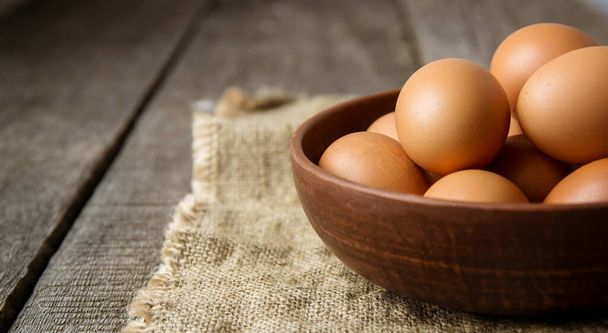 яйца в глиняной тарелке на мешковине и на старом деревянном фоне. копировальное пространство
. - Фото, изображение