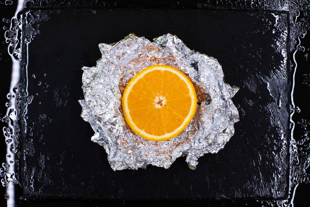 Сочный апельсин нарезанный со скидкой, почерневший на гранитной тарелке с водой
 - Фото, изображение