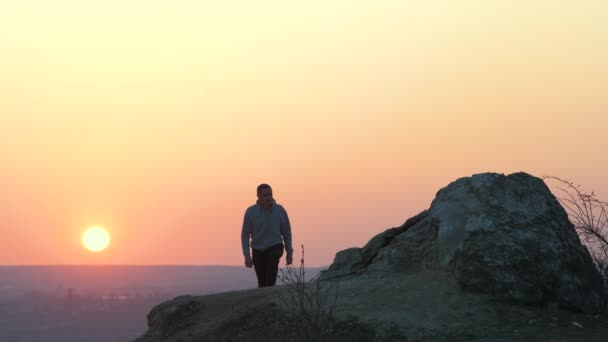 Silhouette egy férfi túrázó mászik egyedül nagy kő naplementekor a hegyekben. Férfi turista felemeli a kezét a magas sziklára az esti természetben. Turizmus, utazás és egészséges életmód koncepció. - Felvétel, videó