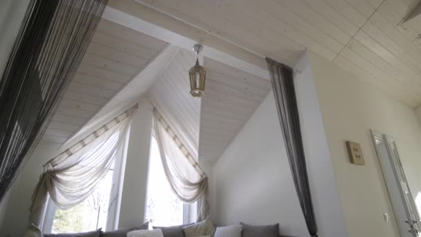 Interior of a modern house spacious hallway with big soft resting place. Contemporary wide sofa with many pillows and light window onder wooden loft ceiling. - Footage, Video