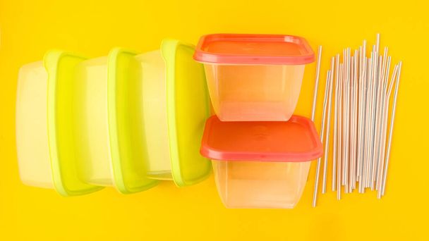 黄色の背景にプラスチック製の弁当箱と飲料ストロー、カラフルなプラスチック容器、カラフルな蓋付きの空のプラスチック食品容器 - 写真・画像