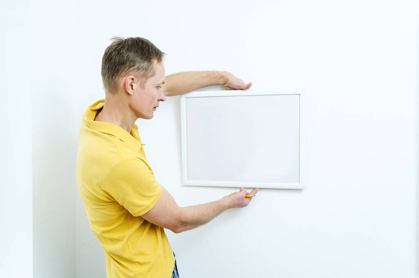 Man is deciding where the picture will hang. - Foto, afbeelding