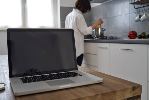 Brunetka kobieta z białą koszulą pracuje w domu z komputerem na stole kuchennym - Zdjęcie, obraz