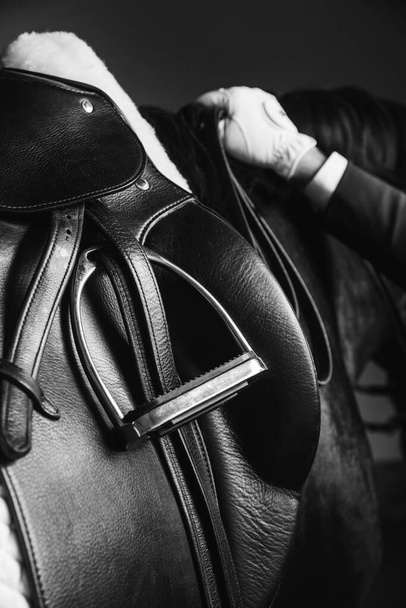Jockey saddle up the thoroughbred horse for dressage or equestrian race. Stirrup, reins and hand on the mane. Noble aesthetics, dress code, professional equipment, competition and excitement concept - Photo, Image