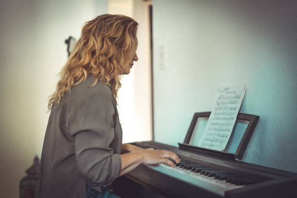 Hübsche Frau spielt an beengten Tagen zu Hause Klavier - Foto, Bild