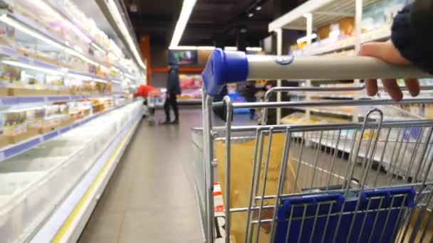 Nerozpoznatelný muž tlačí vozík s výrobky podél řady potravin v supermarketu. Kupující vybírá zboží v obchodě s potravinami. Koncept nakupování. Zpomalený pohyb - Záběry, video