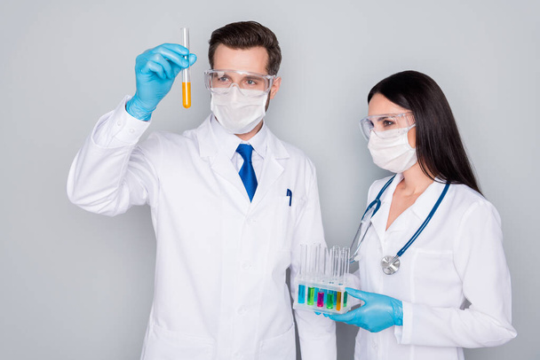 Photo of specialists experienced doc guy lady virology clinic hold blood probe test infection vaccine examining flask wear protect mask gloves lab coat isolated grey color background - Photo, Image