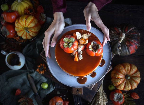 Autumn cake with persimmon and caramel with a pumpkin and a girl in a burgundy dress on a black background, Atmospheric dark food photos, Pastry Homemade - Photo, image
