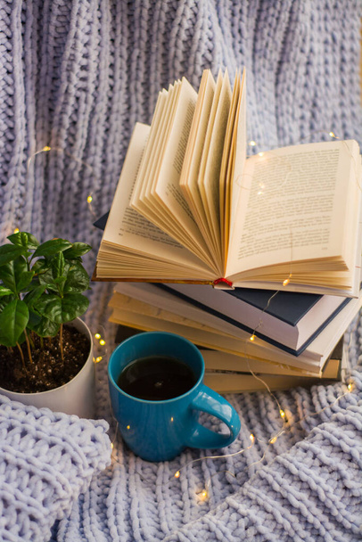 鍋や本、お茶のマグカップ、ガーランドの花と居心地の良い家の中で青いニットプレイと枕の背景。ホームワーク. - 写真・画像
