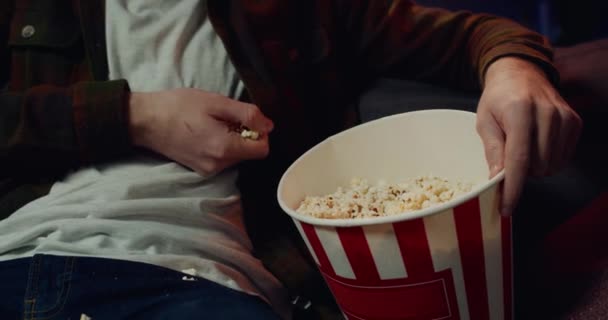 Close up view of male hands grubbing popcorn from paper bowl while watching television. Concept of leisure and entertainment. Indoors. - Video