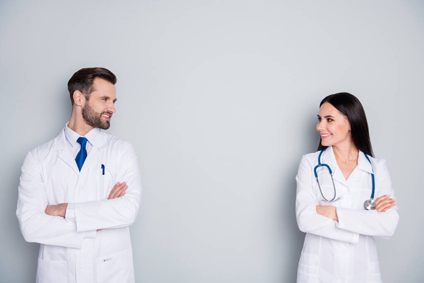 Photo of handsome doc guy lady virology clinic avoid contacting stand meter distance arms crossed experienced doctors look eyes smiling talking wear lab coats isolated grey color background - Photo, Image