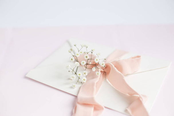 Umschlag auf weißrosa Hintergrund mit pfirsichfarbenem Seidenband und rosa Blüten. Hochzeitseinladung. Muttertagskarte. Platz für Text. Kopierraum. - Foto, Bild