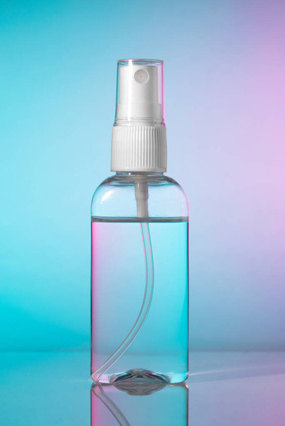 Eine kleine Flasche antibakterielles Händedesinfektionsmittel Alkoholnebel Spray. Antiseptische Flüssigkeit in transparentem Kunststoffbehälter mit weißer Zerstäuberpumpe auf blauem Magenta-Hintergrund, ohne Etikett. - Foto, Bild