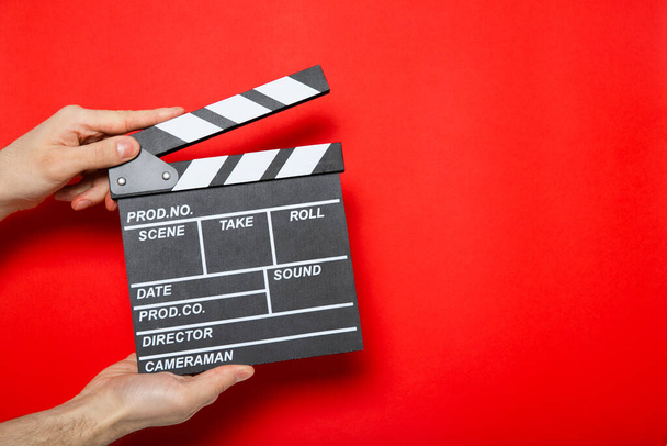 Κλαπέτα ταινίας στα χέρια ενός άντρα σε κόκκινο φόντο με θέση για κείμενο - Φωτογραφία, εικόνα