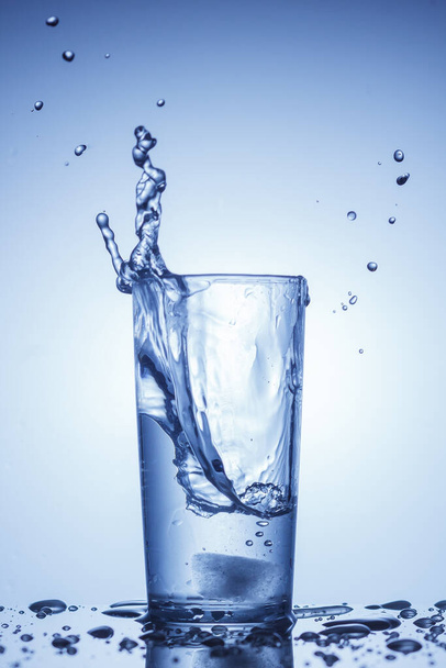 Een plons water in een glas in blauw - Foto, afbeelding