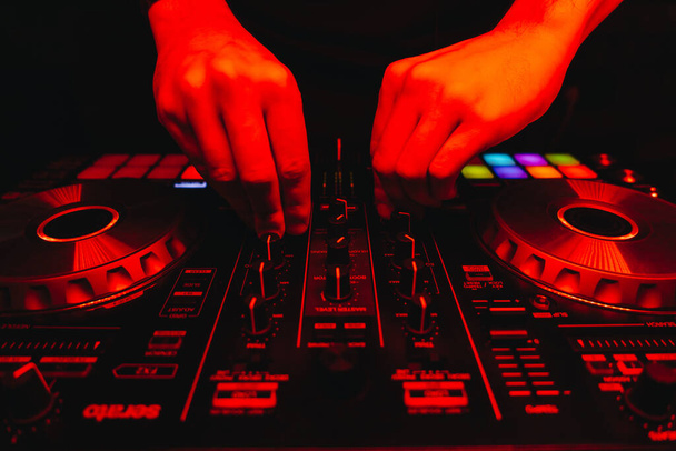 DJ está ligando os interruptores do controlador de perto na luz vermelha da boate, mãos masculinas visíveis
 - Foto, Imagem