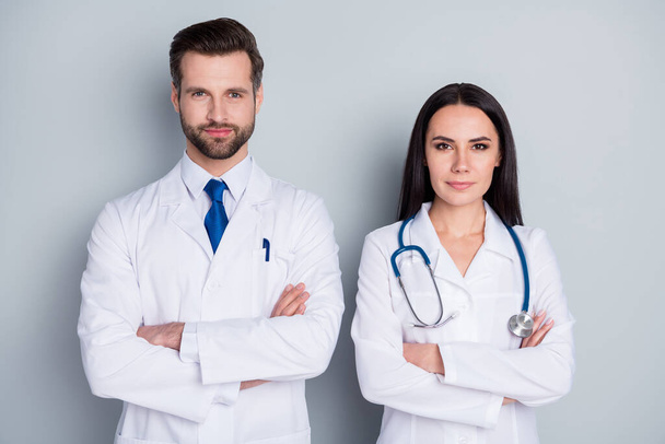 Photo of handsome doc guy professional lady patients consultation virology clinic listen client complaining arms crossed confident doctors wear lab coats isolated grey color background - 写真・画像