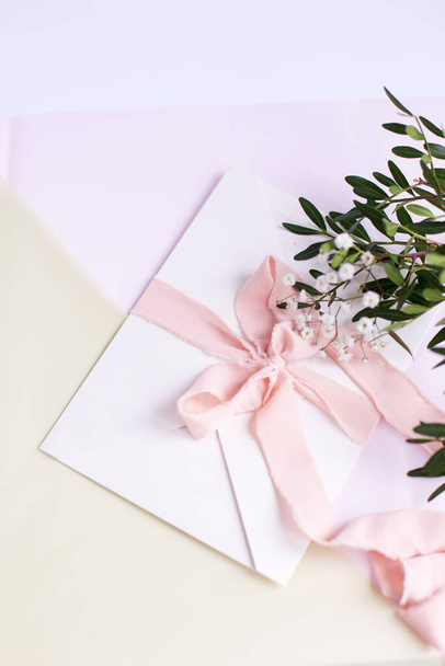 Envelope sobre um fundo branco-rosa com fita de seda de pêssego, ramo verde e flores. Um convite de casamento. O cartão da mãe. Lugar para SMS. Espaço de cópia
. - Foto, Imagem
