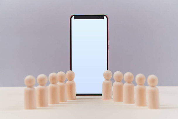 Smartphone moderno y figuras de madera maqueta. Pantalla de teléfono celular con espacio de copia, miniaturas de personas. Concepto de redes sociales
 - Foto, imagen