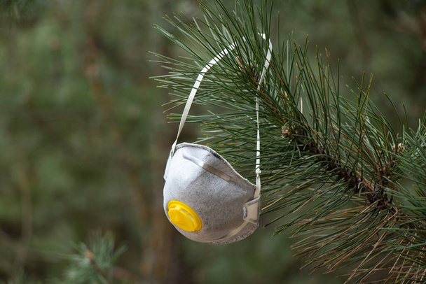 Medizinische Maske hängt an den Ästen eines Weihnachtsbaums im Wald - Foto, Bild