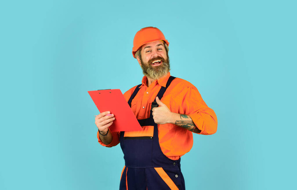 Foreman with document. Delivering building materials. Man in hard hat holding clipboard looking information. Buy materials for renovation. Bearded storekeeper. Checklist. Inspecting. Control concept - Фото, зображення