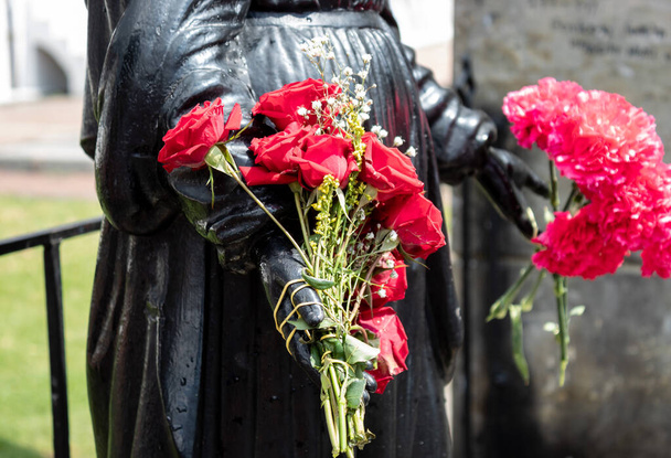 Закрытый к статуе Черной Девы руки внутри кладбища с красными розами и красными цветами в руках
. - Фото, изображение