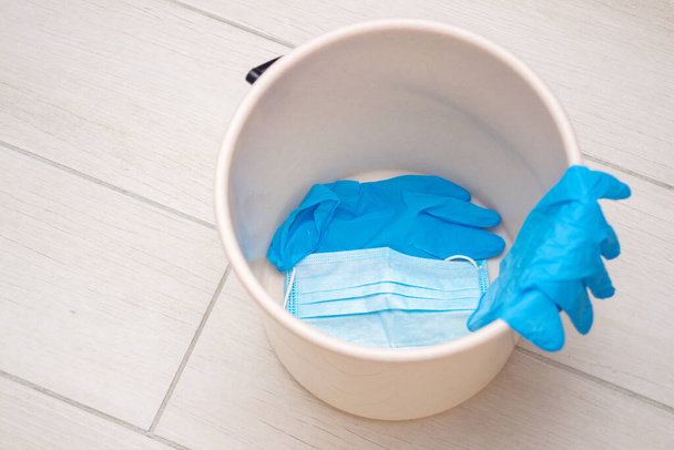 Kullanılmış mavi tıbbi lateks eldivenler ve çöp kutusunda tek kullanımlık koruyucu maskeler. Bulaşıcı kişisel koruyucu ekipmanların imhası sorunu. Coronavirus salgını ve enfeksiyon bulaşma konsepti - Fotoğraf, Görsel