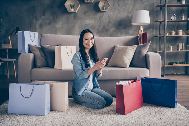 Profile photo of domestic pretty asian lady relaxing sit comfy floor carpet couch stay home quarantine time making online shopping telephone app many packs living room indoors - Foto, imagen