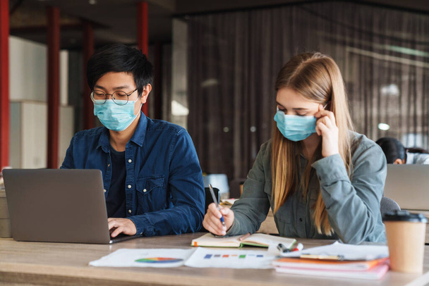 Photo of multinational young students in medical masks studying with laptop at classroom - Photo, image