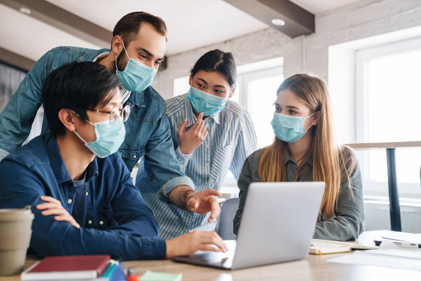 Photo of multinational young students in medical masks studying with laptop at classroom - Фото, зображення