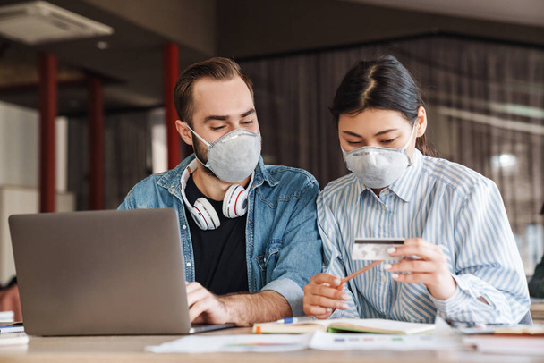 Photo of multinational nice students in medical masks holding credit card while studying at classroom - Fotografie, Obrázek